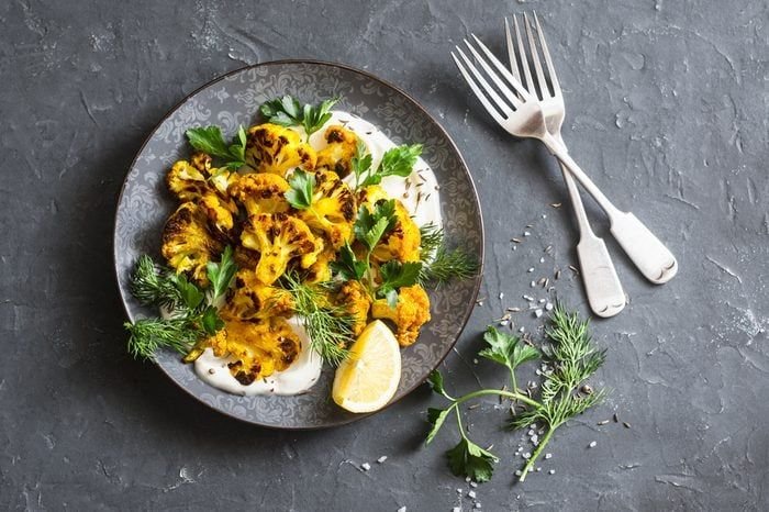Roasted turmeric cauliflower with greek yogurt dressing. Delicious healthy snack on a dark background, top view