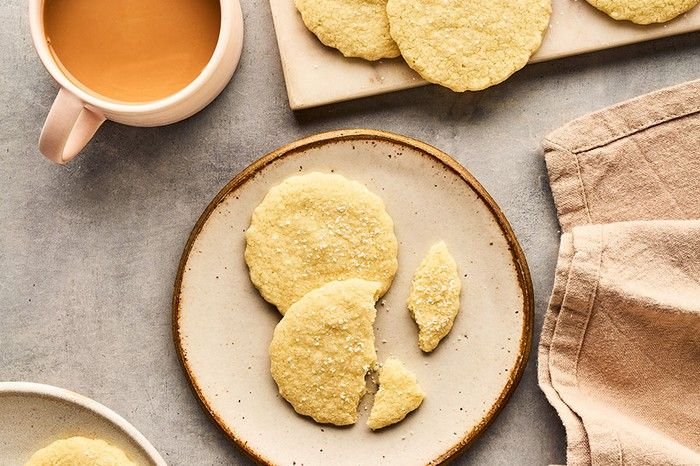 A board and two plates of shortbread biscuits next to a tea towel and cup of tea